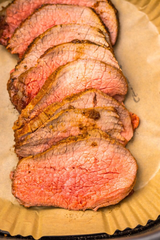 Several slices of medium-rare roast beef arranged in a row on brown parchment paper.