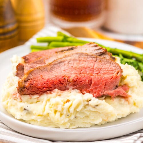 Two slices of medium-rare steak served on mashed potatoes with a side of asparagus on a white plate.