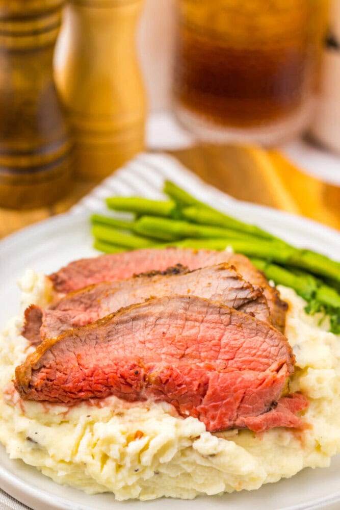 Three slices of medium-rare roast beef on mashed potatoes, served with green beans on a white plate.