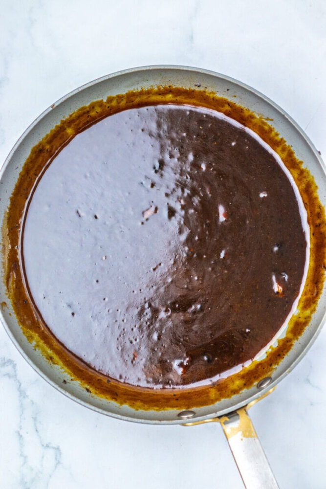 A metal pan containing a dark brown sauce or glaze sits on a light-colored marble surface.