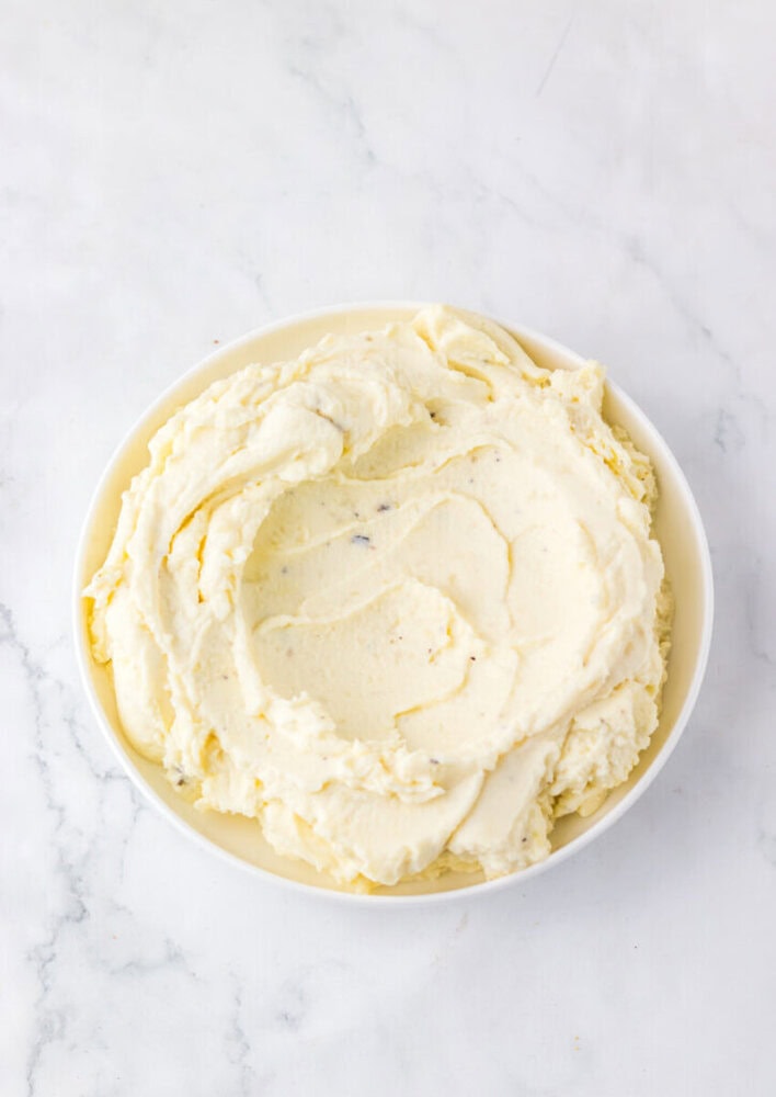 A white bowl filled with smooth, creamy mashed potatoes on a marble surface.