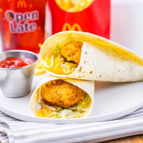 Two chicken snack wraps with lettuce and cheese on a plate, served with ketchup, fries, and a soft drink in McDonald’s packaging.