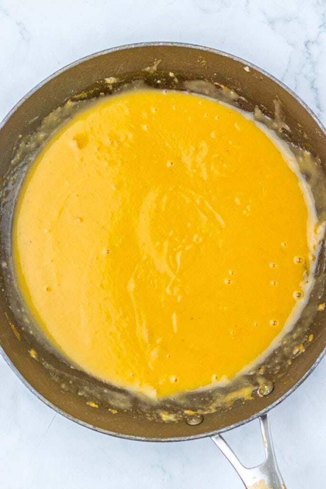 A skillet filled with smooth, yellow cheese sauce on a light-colored surface.