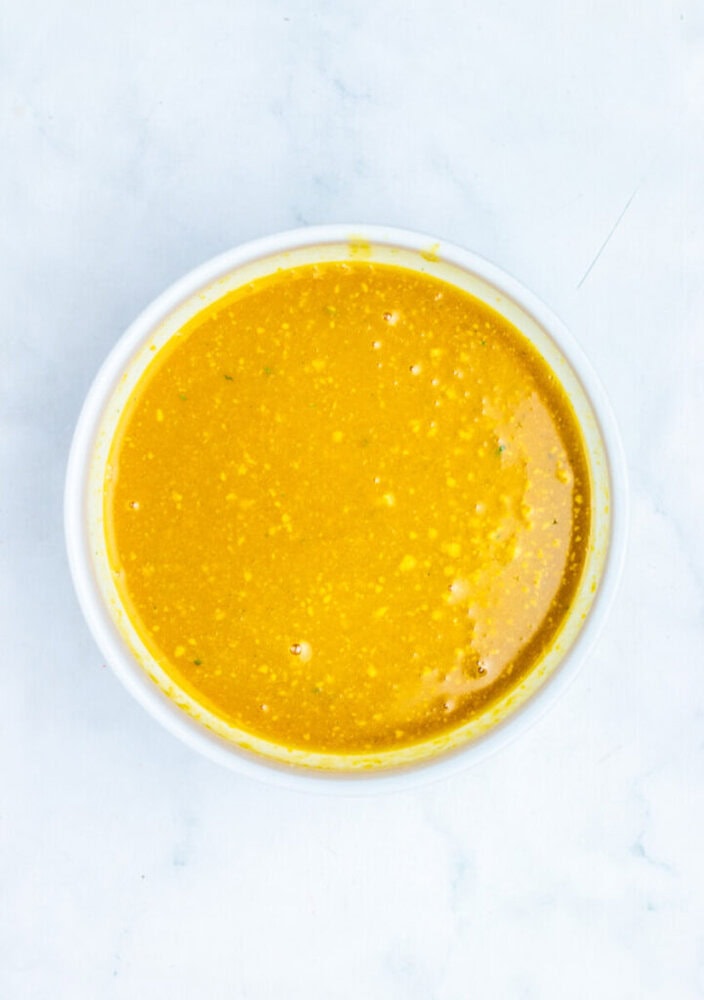 A white bowl filled with a yellow, slightly textured liquid sauce or dressing, placed on a white marble surface.