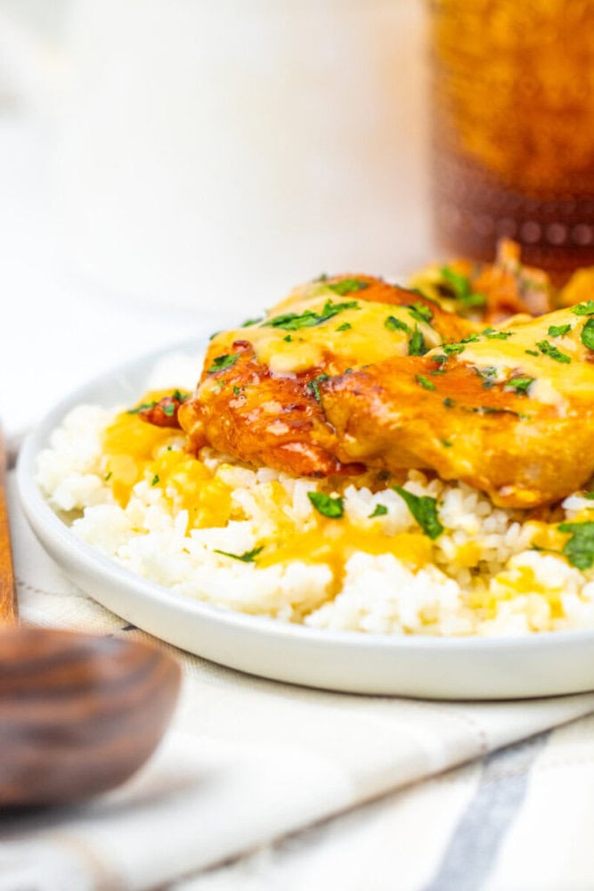 A plate of white rice topped with saucy chicken pieces and garnished with chopped herbs.