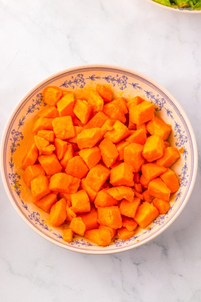A bowl filled with cubed, cooked orange sweet potatoes sits on a marble surface.
