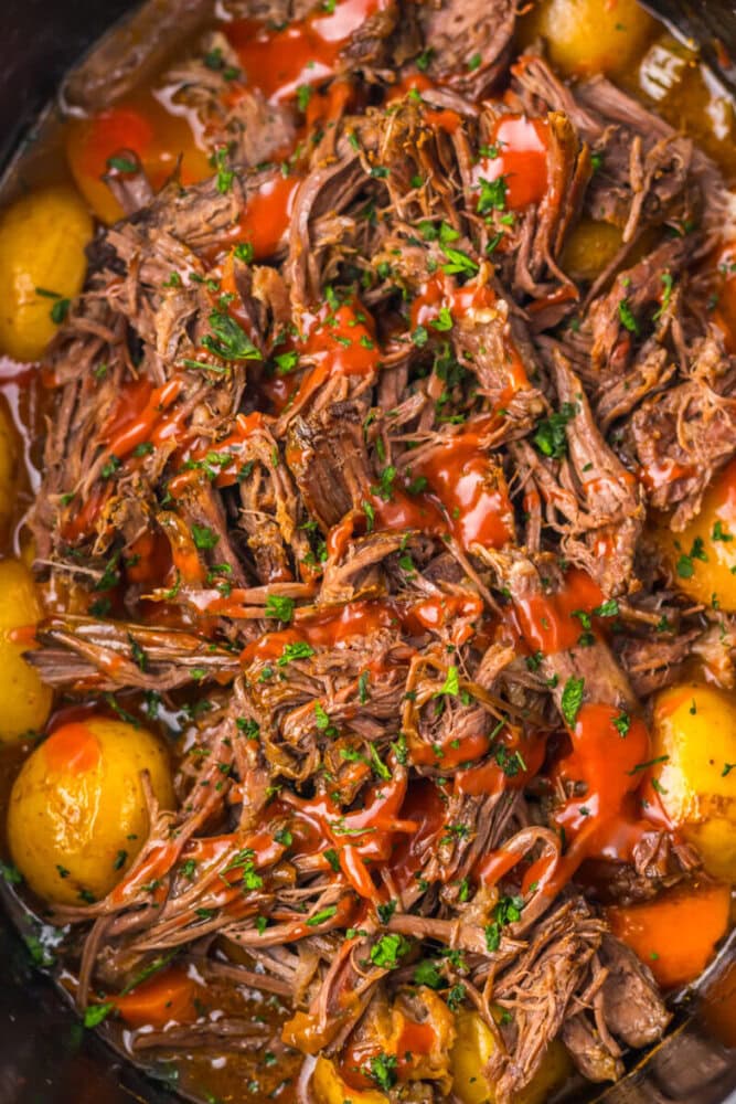 Shredded pot roast with baby potatoes, garnished with chopped herbs and drizzled with red sauce.