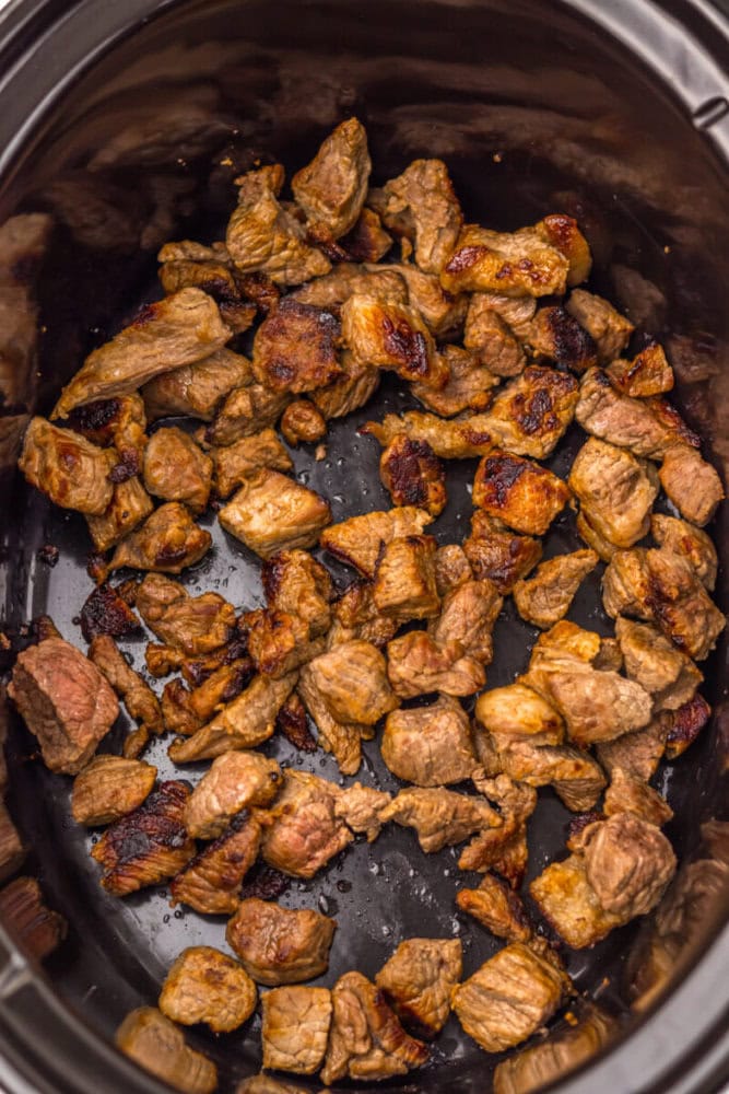Cubed beef pieces browned and cooked in a slow cooker, showing a mixture of seared edges and tender meat.