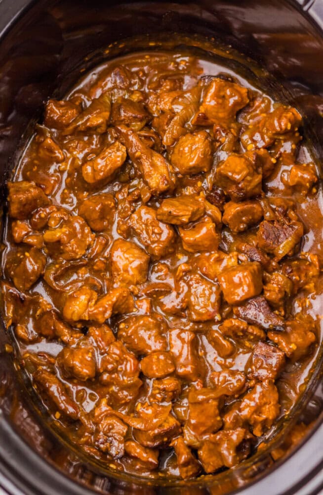 Chunks of beef coated in a thick brown sauce inside a slow cooker.