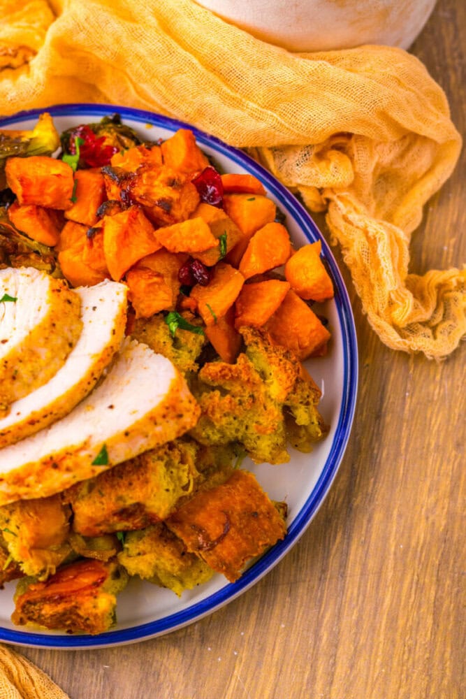 A plate with sliced roasted turkey, stuffing, and roasted sweet potatoes on a wooden table with a yellow cloth.