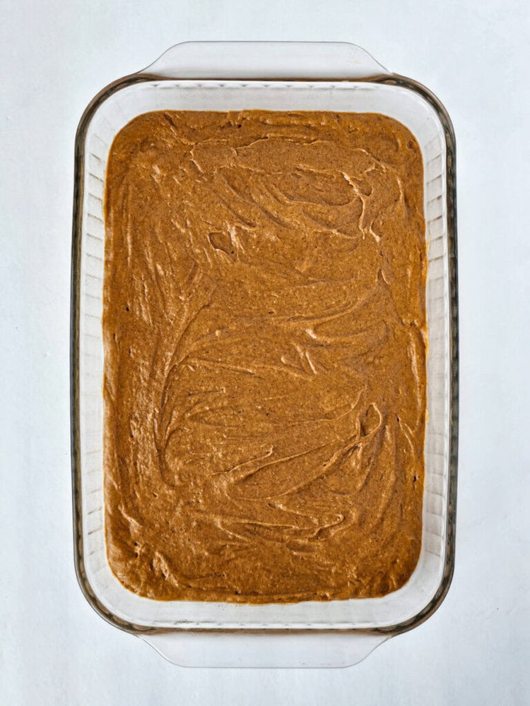 A glass baking dish filled with an even layer of light brown batter on a white surface.
