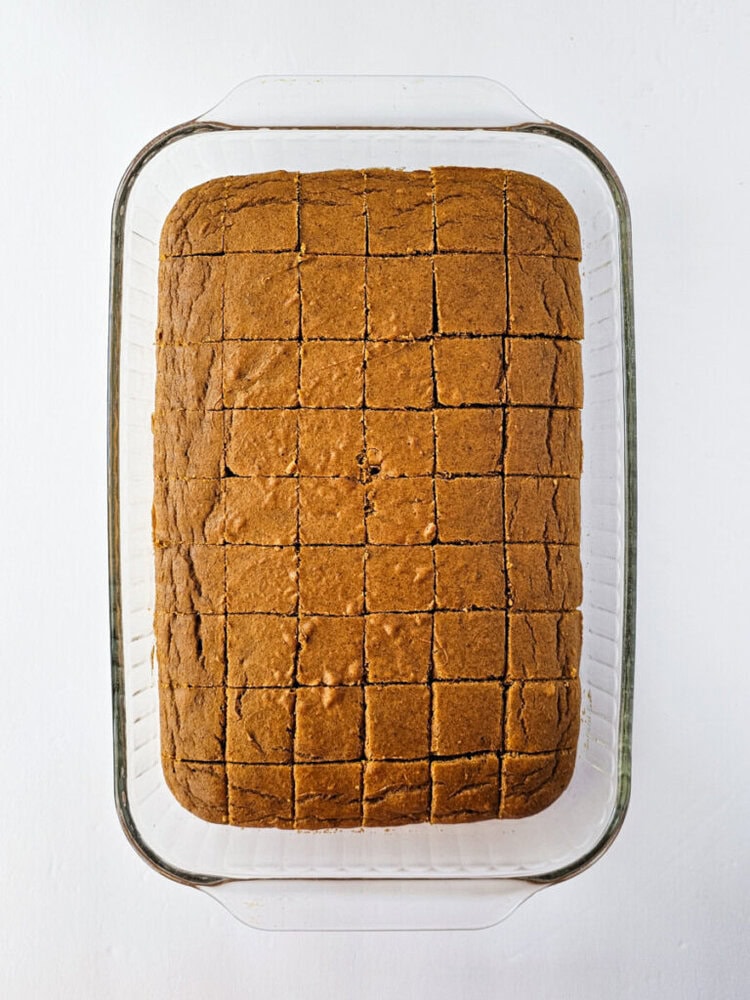 A rectangular baked dessert in a glass dish is cut into small, even squares, viewed from above on a white background.
