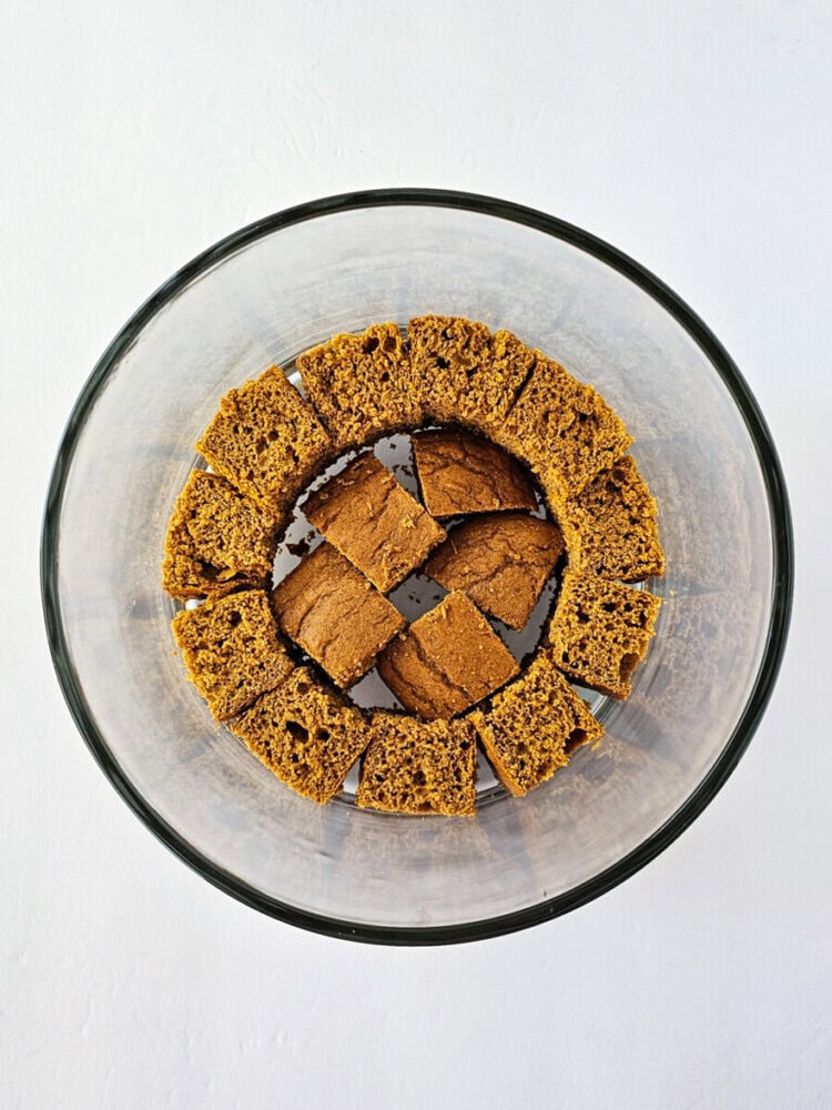 A glass bowl with an even layer of square and rectangular pieces of brown cake or bread arranged in a circular pattern.