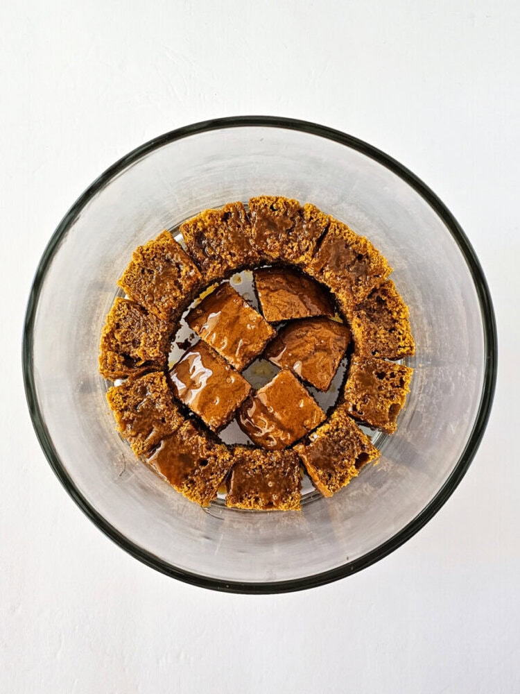 A glass bowl containing square pieces of brown cake arranged in two circular layers against a white background.