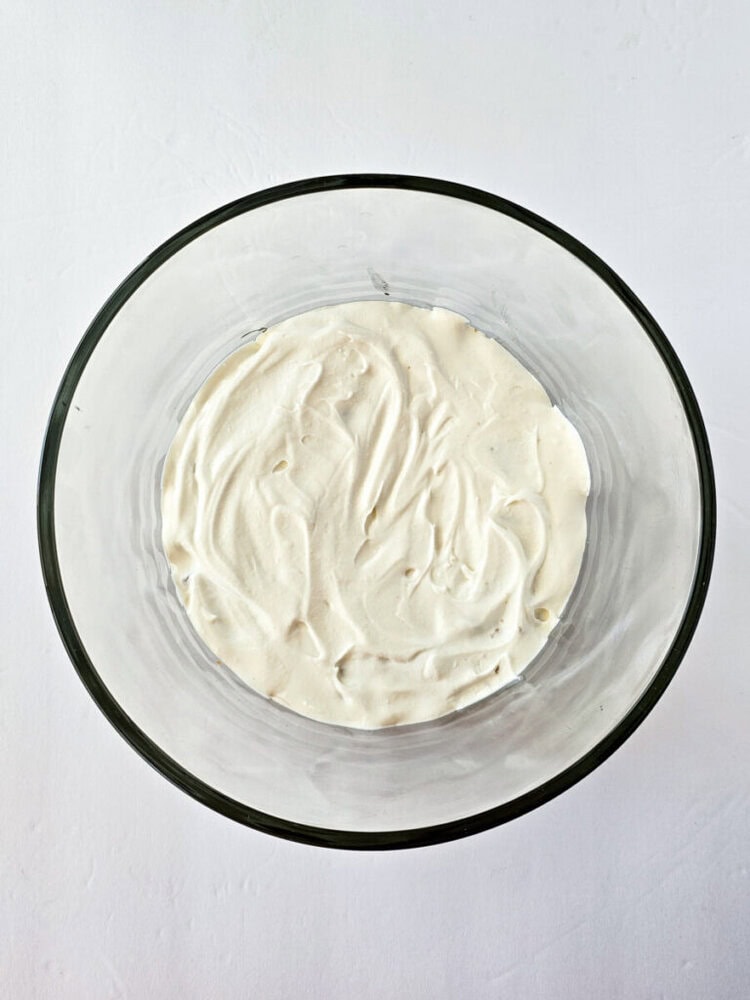 A glass bowl containing a smooth, white creamy mixture on a white surface.