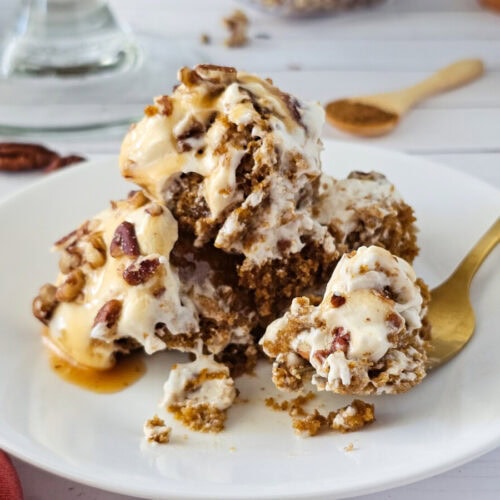 A serving of pecan pie ice cream dessert on a white plate with a gold spoon, sitting on a white wooden table.