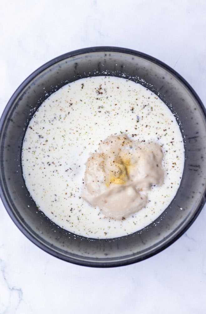 A black bowl filled with white liquid, a dollop of thick beige mixture, and sprinkled black pepper on top, placed on a white surface.
