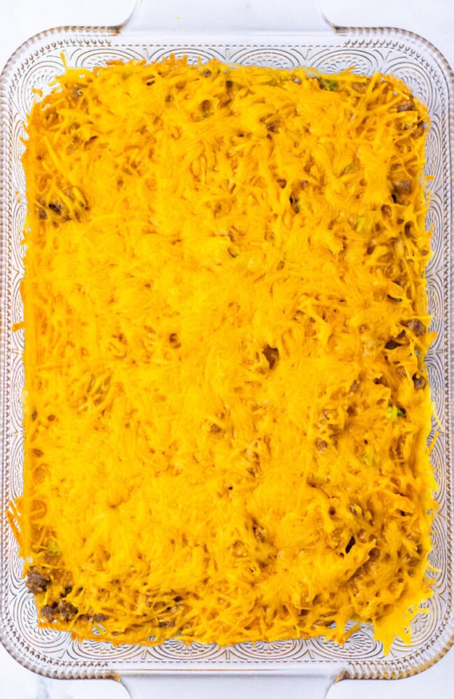 Rectangular glass baking dish filled with a casserole topped with a melted layer of shredded cheddar cheese.