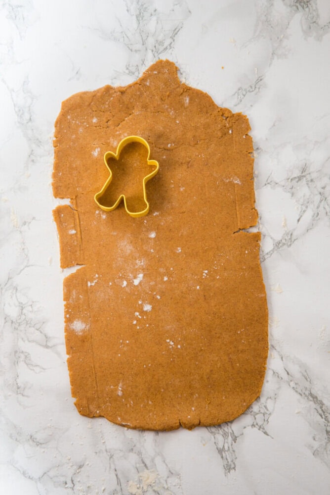 Rolled out gingerbread dough on a marble surface with a yellow gingerbread person cookie cutter placed on top.