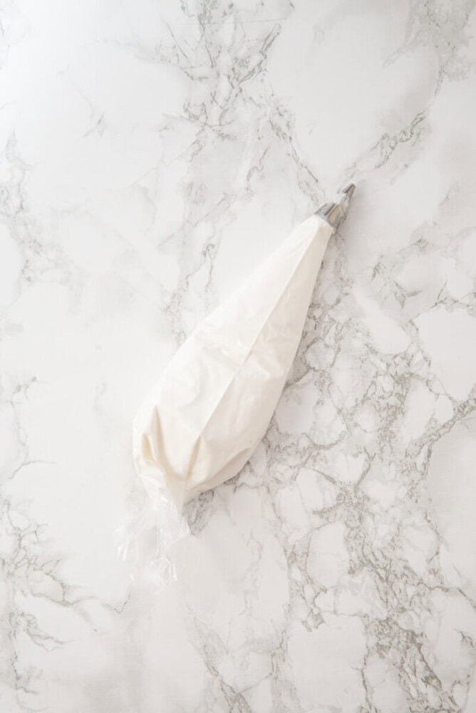 A piping bag filled with white frosting is placed on a white marble surface.