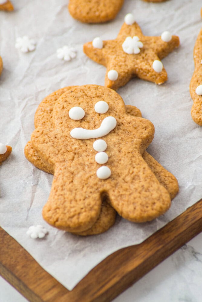 A gingerbread man cookie decorated with white icing sits on parchment paper next to a star-shaped cookie and small snowflake decorations.