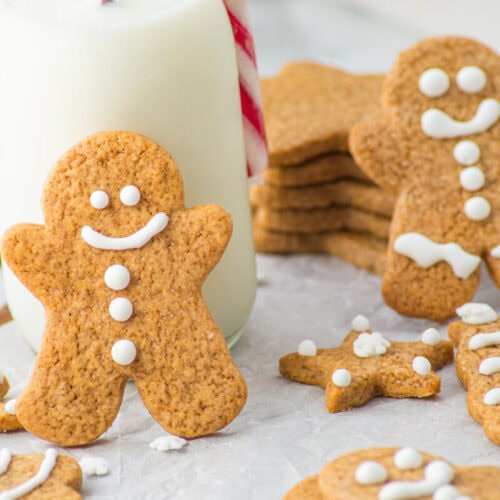 Gingerbread cookies decorated with white icing are arranged on a table next to a glass of milk with a red and white striped straw.