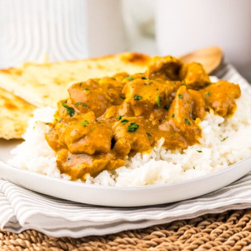 A plate of white rice topped with chicken curry, garnished with herbs, served with naan bread on the side.