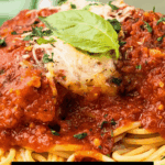Spaghetti topped with tender Slow Cooker chicken parmesan, marinara sauce, grated cheese, and a fresh basil leaf.