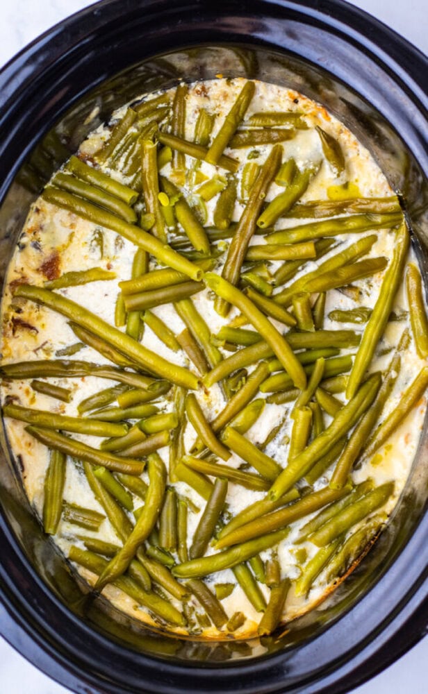 Green beans in a creamy sauce inside a slow cooker, viewed from above.