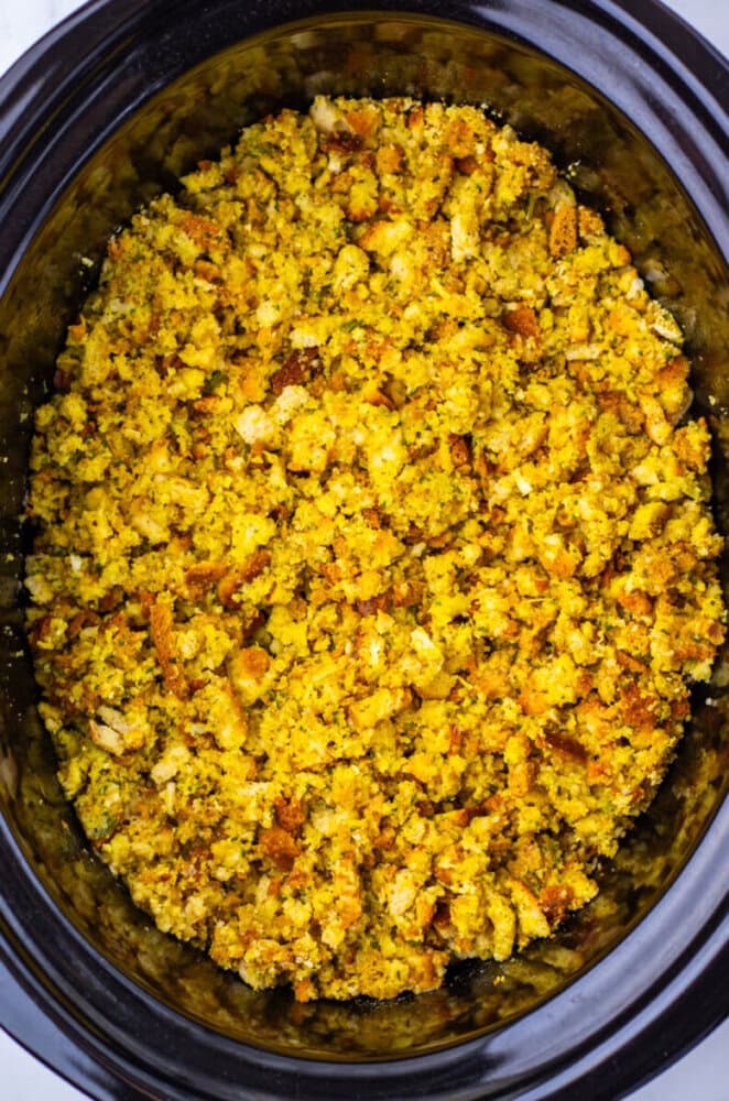 A close-up view of cornbread stuffing in a black slow cooker, showing a crumbly, golden-brown texture.