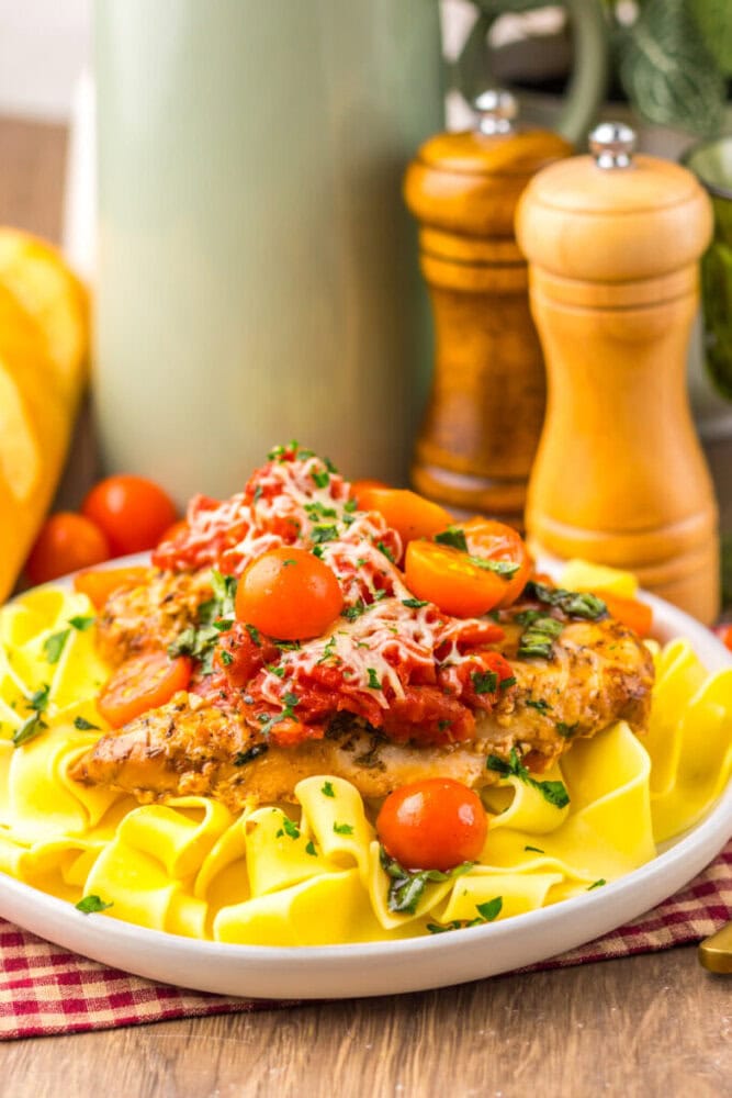 A plate of pasta topped with breaded chicken, marinara sauce, cherry tomatoes, and grated cheese, with salt and pepper shakers in the background.