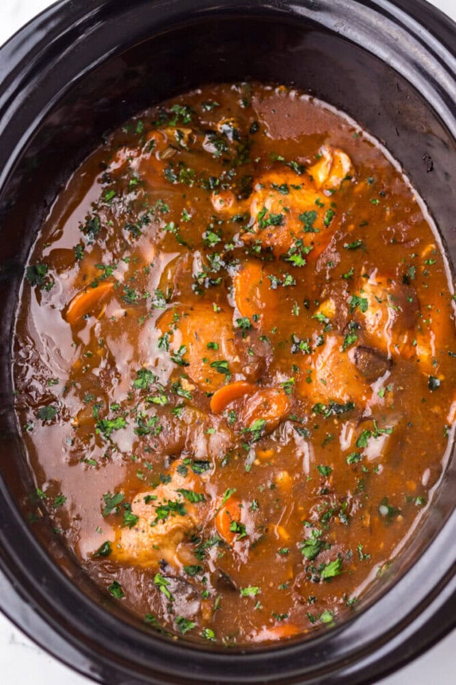 Chicken stew with carrots and herbs in a thick brown sauce, cooked in a black slow cooker.