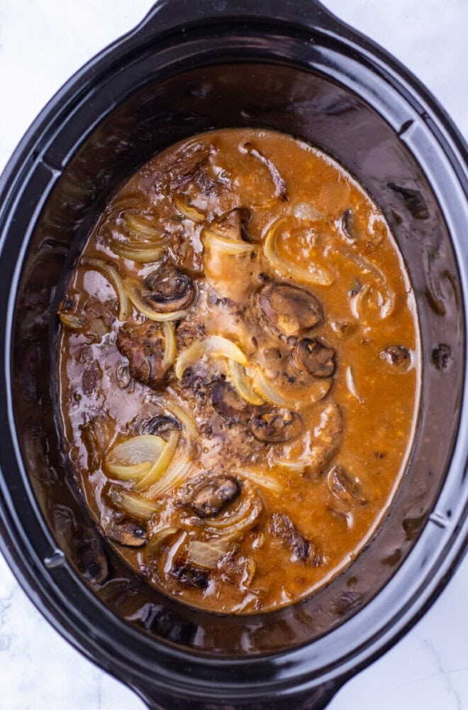 Beef patties in brown gravy with onions and mushrooms cooking in a slow cooker.