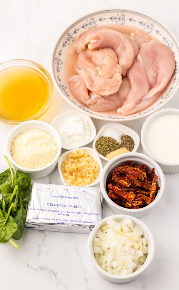 Ingredients for a chicken recipe arranged on a countertop, including chicken, cream, broth, herbs, and vegetables.