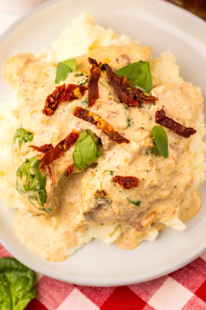 Chicken in creamy sauce with spinach and sun-dried tomatoes served over mashed potatoes on a white plate.