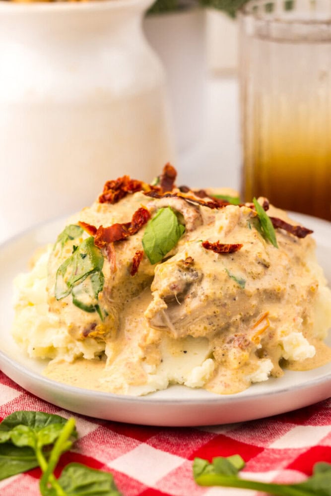 Chicken in a creamy sauce with spinach and sun-dried tomatoes served over mashed potatoes on a white plate.
