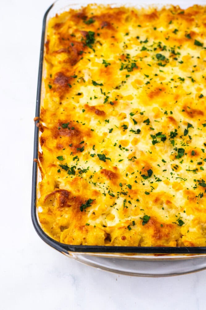 A glass baking dish filled with baked macaroni and cheese, topped with melted, golden-brown cheese and sprinkled with chopped herbs.