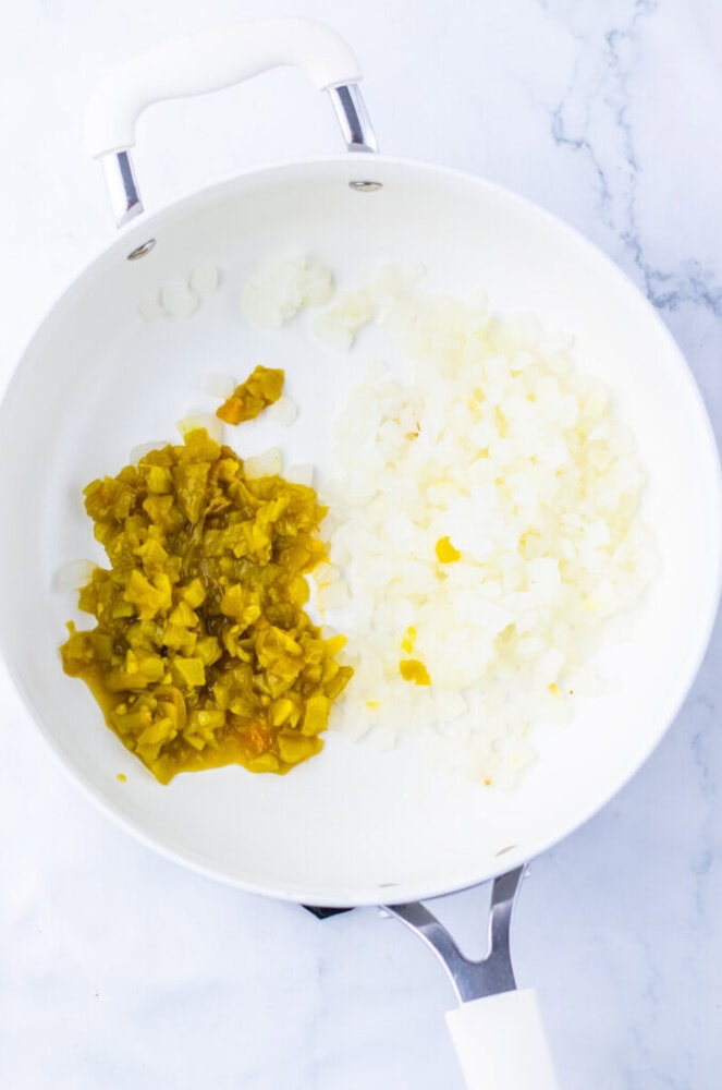 A white skillet on a marble surface contains diced yellow-green peppers and chopped onions, separated into two sections.