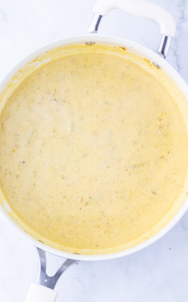 A white saucepan filled with a creamy yellow sauce, resting on a light marble surface.