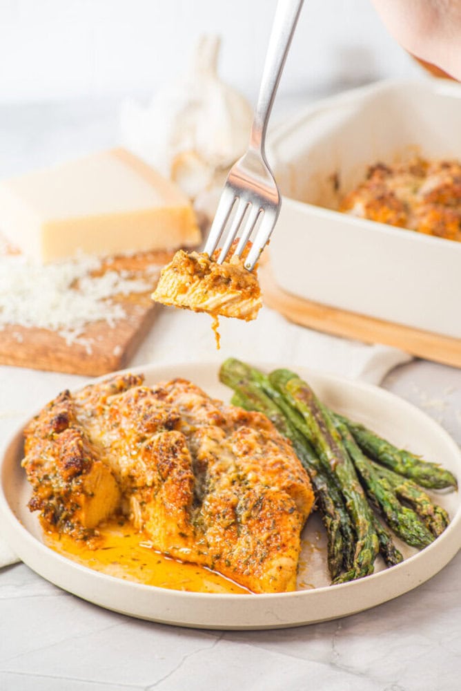 A plate with baked chicken, roasted asparagus, and a fork holding a piece of chicken above the plate.