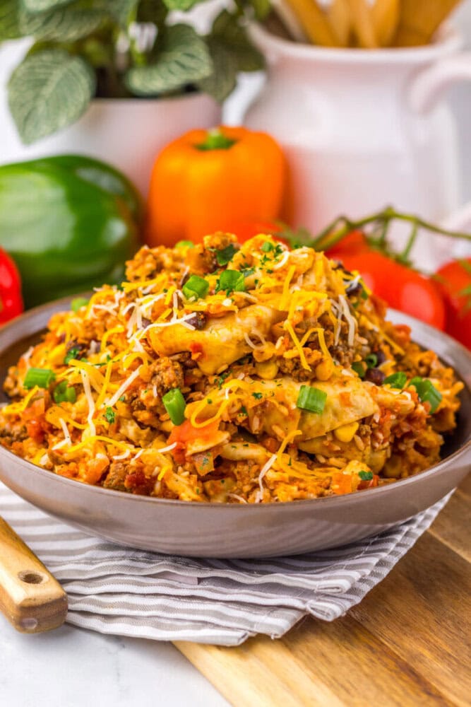 A bowl of cheesy taco pasta with ground beef, topped with shredded cheese and green onions.