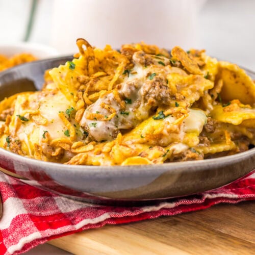A bowl of cheesy pasta casserole with ground beef and crispy onions on a red checkered napkin.