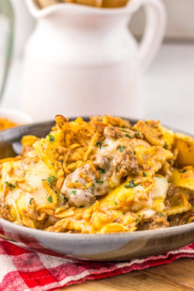 A bowl of cheesy baked casserole with ground meat, pasta, and crispy fried onions on top.