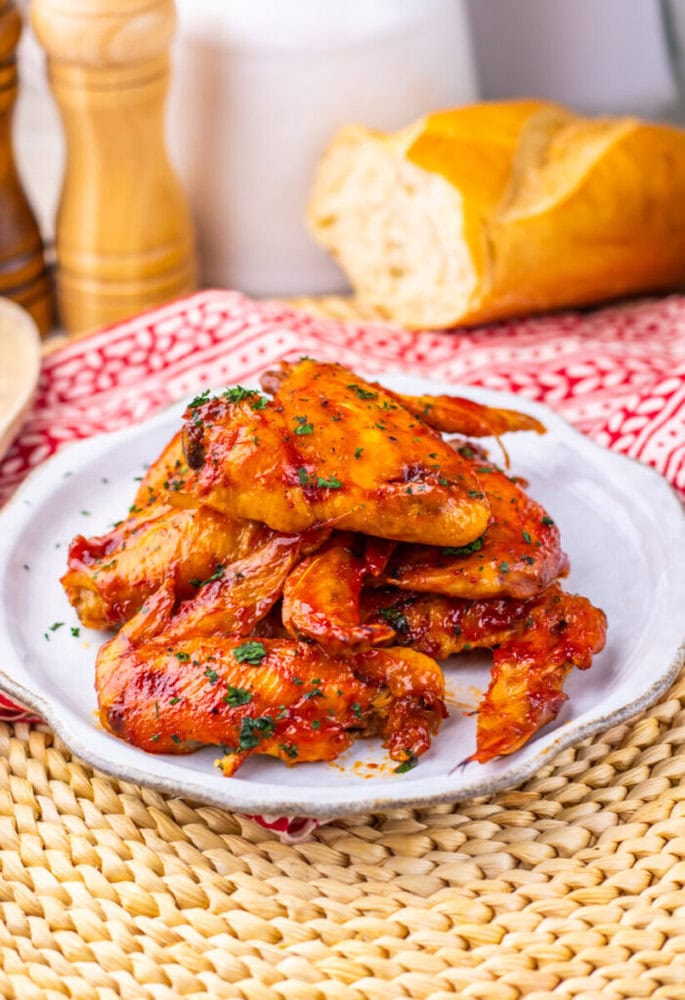 A plate of glazed chicken wings garnished with herbs, with bread and seasonings in the background.