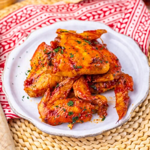 A plate of saucy chicken wings garnished with herbs, on a white plate with a red patterned napkin.