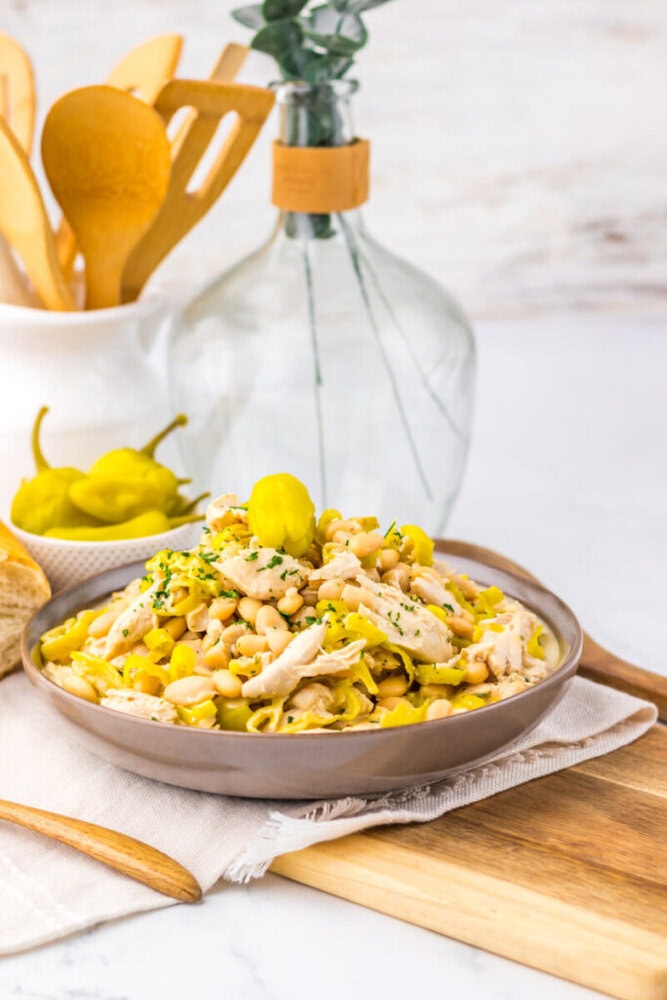 A bowl of white bean and shredded chicken salad garnished with pepperoncini on a wooden board.
