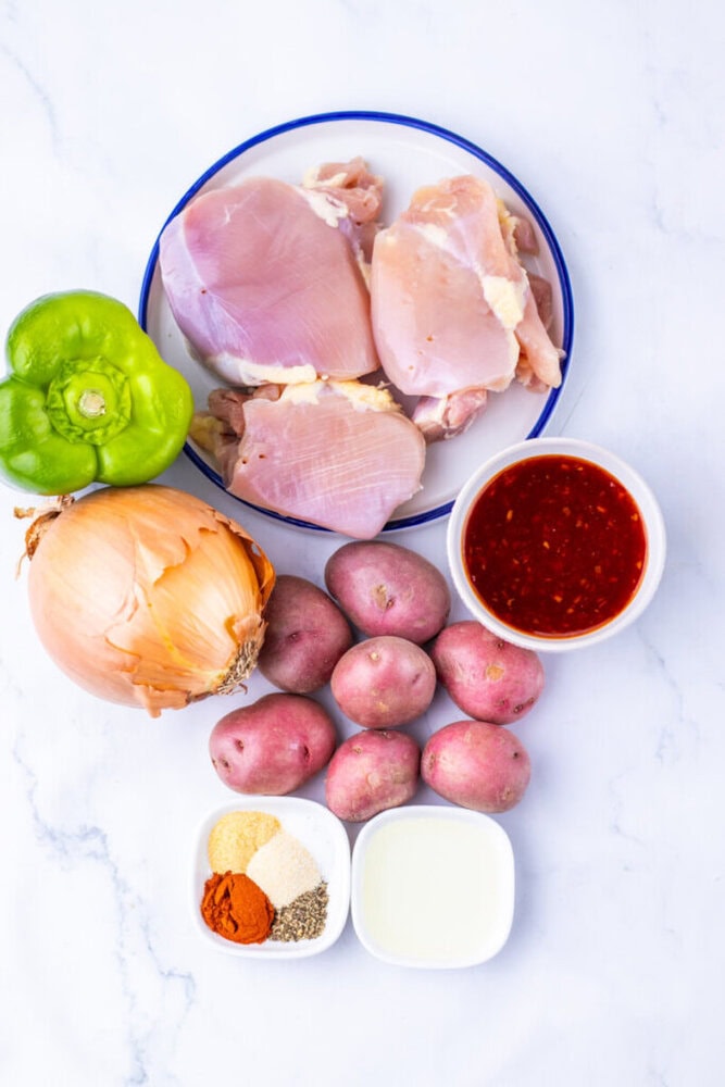 Raw chicken, green bell pepper, onion, red potatoes, red sauce, milk, and spices on a white background.