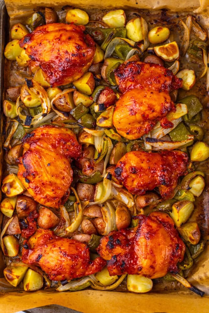 Roasted chicken thighs with potatoes, onions, and peppers on a baking sheet, cooked and golden brown.
