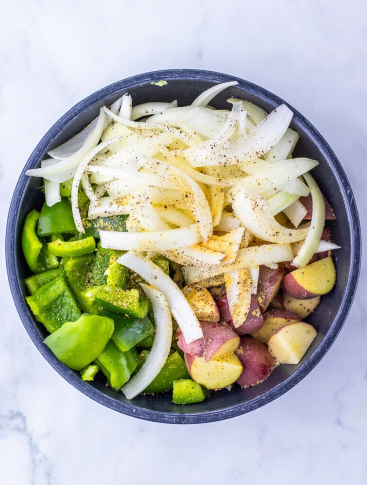 A bowl with sliced onions, green bell peppers, and chopped red potatoes, lightly seasoned.