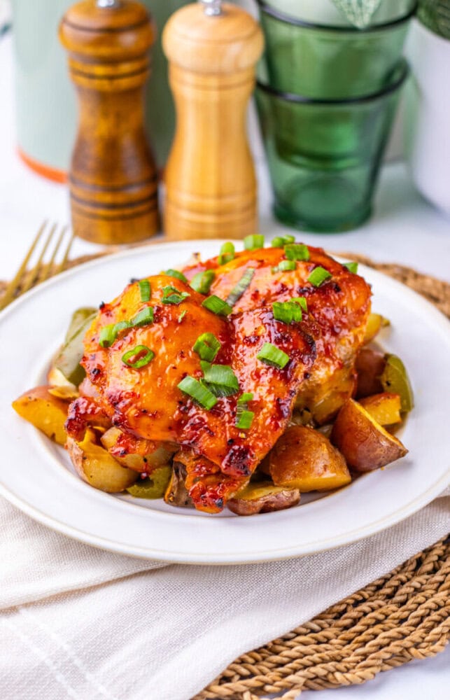 A plate of glazed baked chicken with chopped green onions and roasted potatoes, with salt and pepper shakers behind.